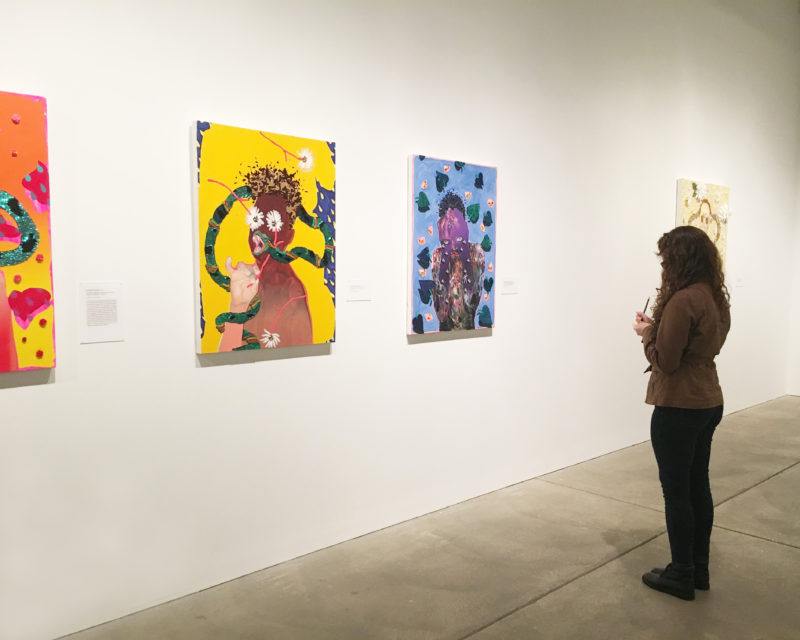 A woman looks at artwork while taking notes.