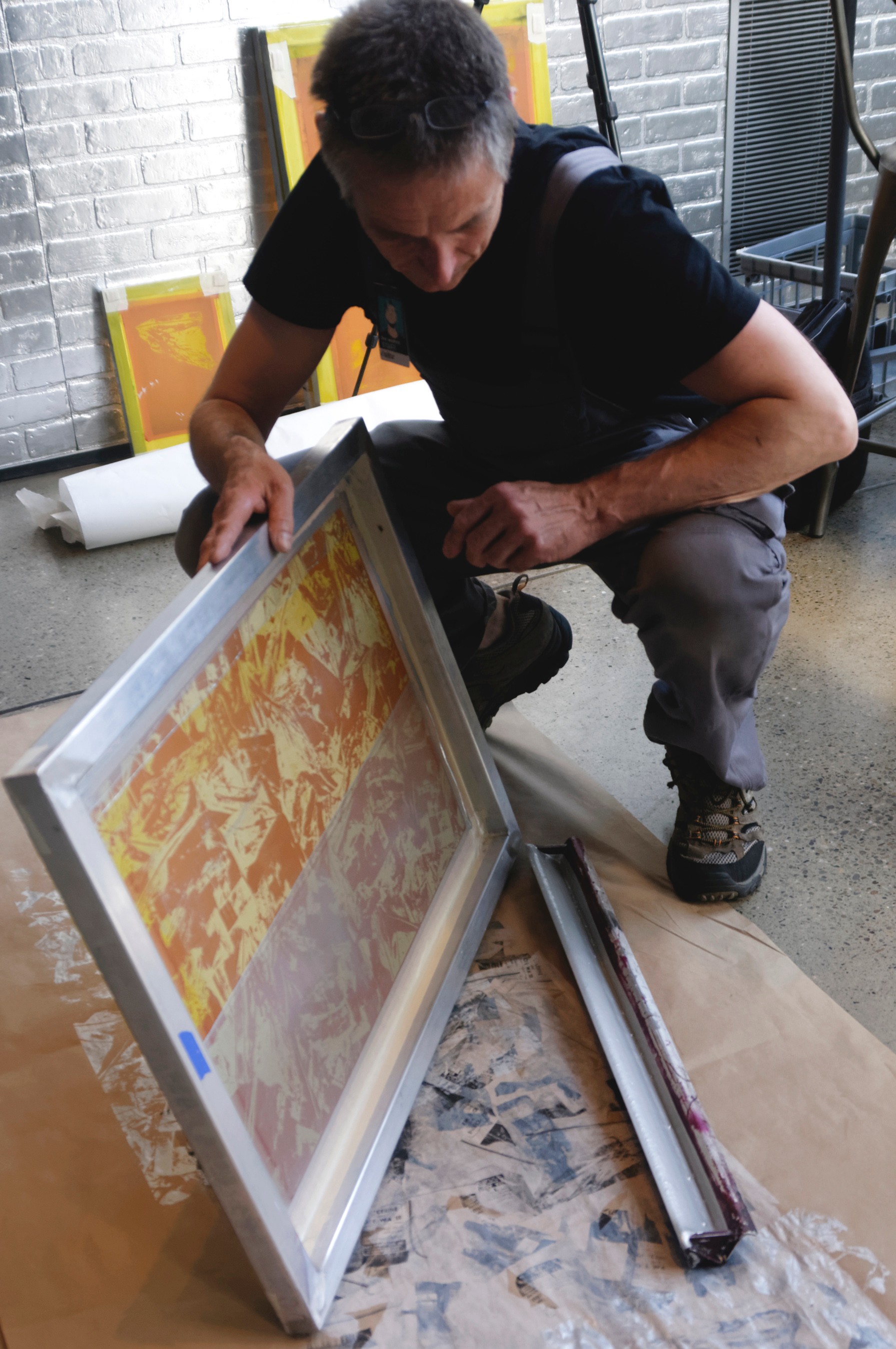 Stephen Hoffman is crouched down, assembling a silver frame for one of his pieces of artwork.