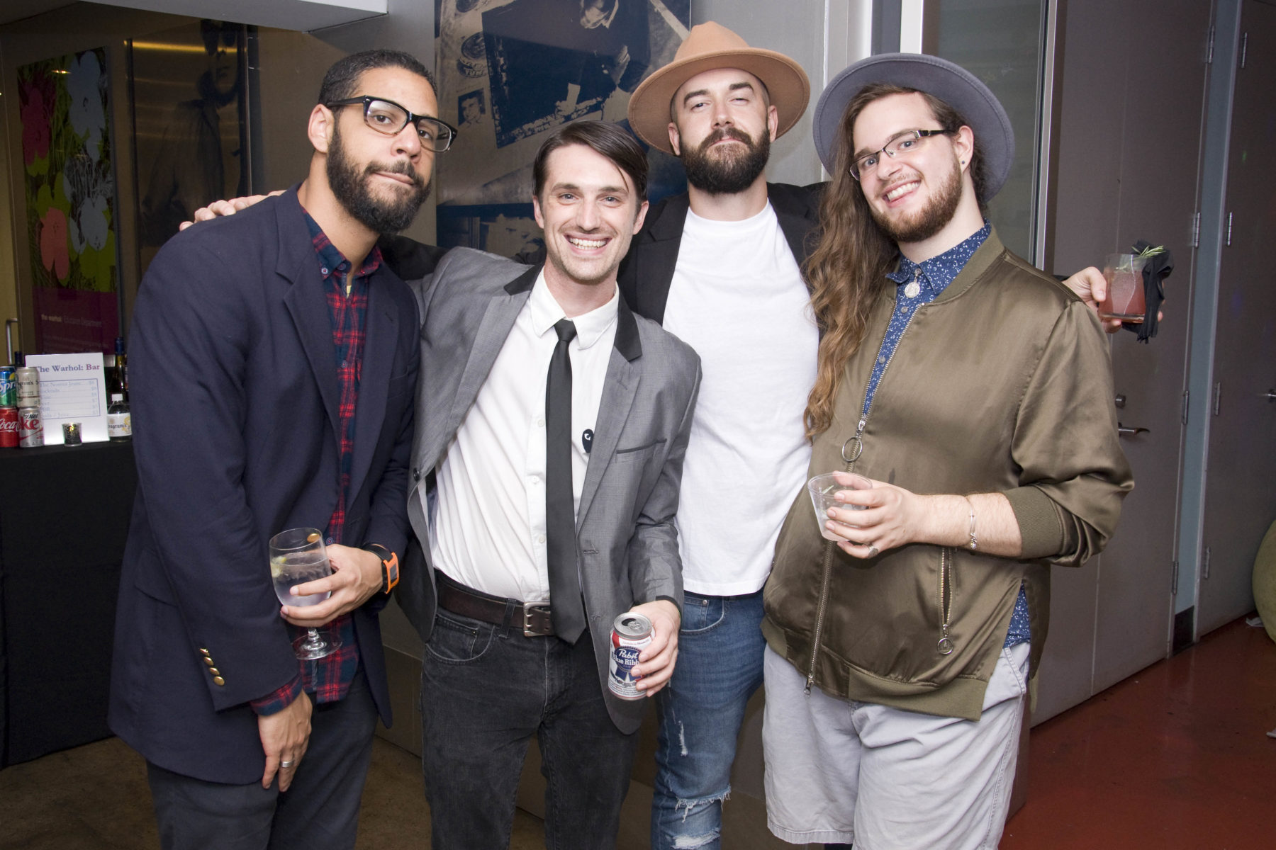 Four men, dressed wearing skinny ties and hats, pose for a photo during the Night of 1000 Elvises fundraiser. They wear large smiles on their face.