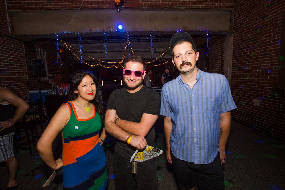 A woman stands with two men. They are all smiling and looking at the camera.